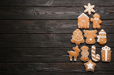 Photo of Christmas tree shape made of delicious gingerbread cookies on black wooden table, flat lay. Space for text