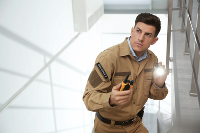 Photo of Professional security guard with portable radio set and flashlight on stairs