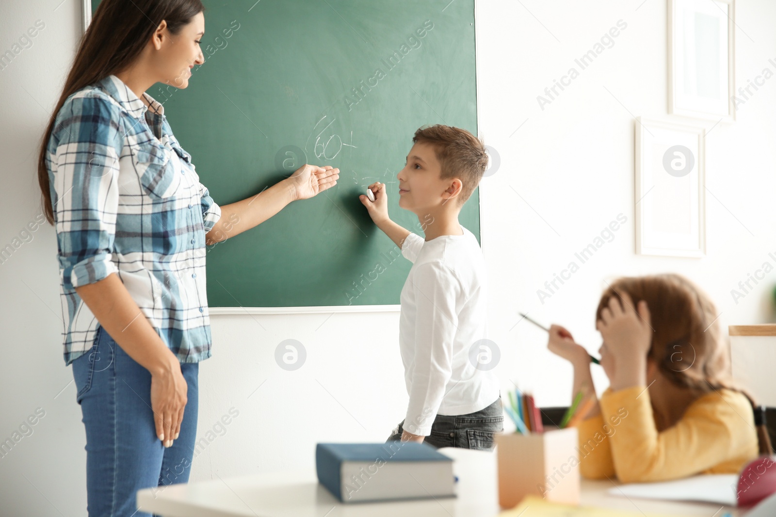 Photo of Young teacher and boy near chalkboard in classroom