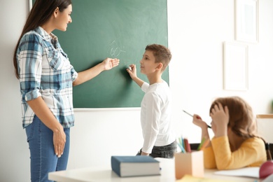 Photo of Young teacher and boy near chalkboard in classroom