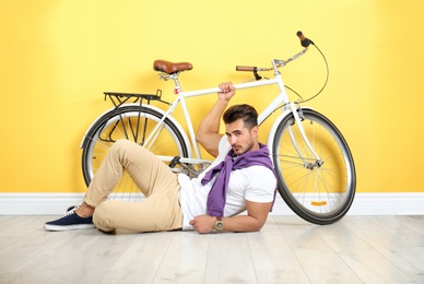 Photo of Handsome young hipster man lying with bicycle near yellow wall