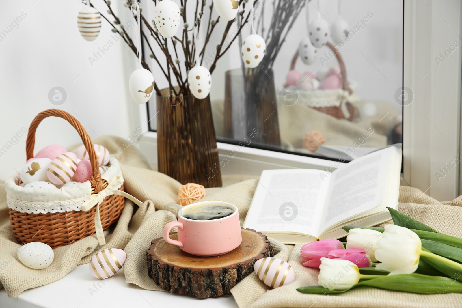 Photo of Easter decorations. Cup of coffee, painted eggs, tulips and book on windowsill