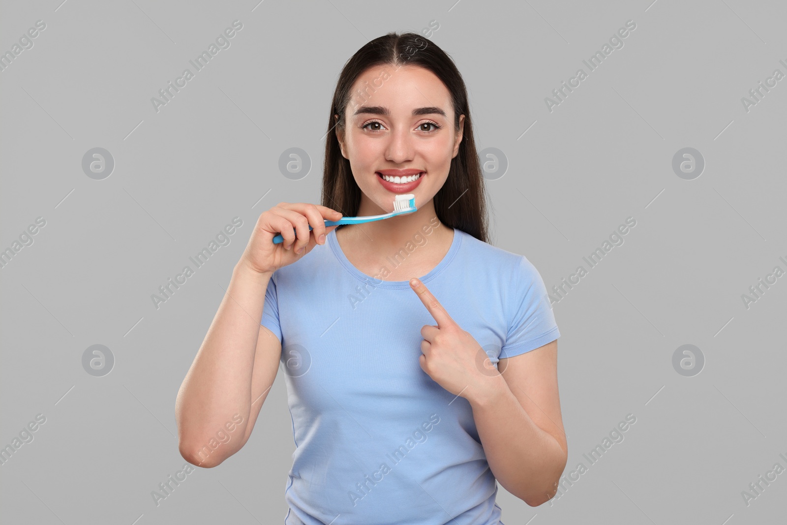 Photo of Happy young woman holding plastic toothbrush on light grey background