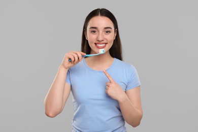 Happy young woman holding plastic toothbrush on light grey background