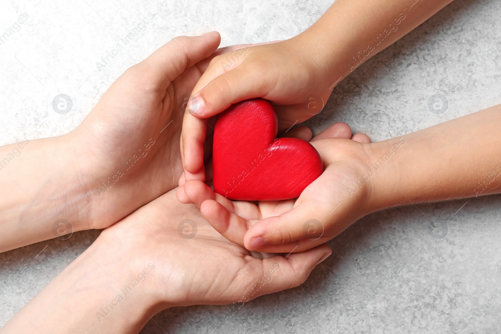 Photo of Closeup of woman and child holding heart on grey stone background, top view. Donation concept