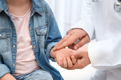 Photo of Doctor checking little girl's pulse with fingers on light background, closeup
