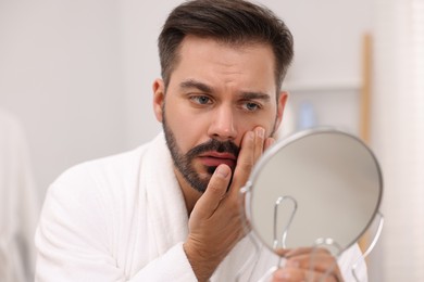 Man with skin problem looking at mirror indoors