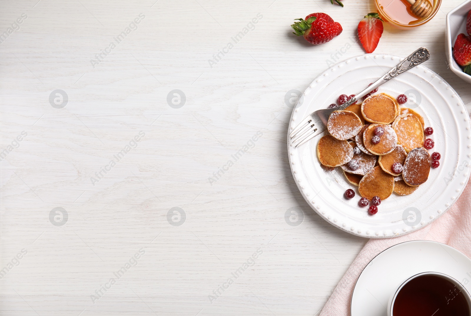 Photo of Delicious mini pancakes cereal with cranberries served on white wooden table, flat lay. Space for text