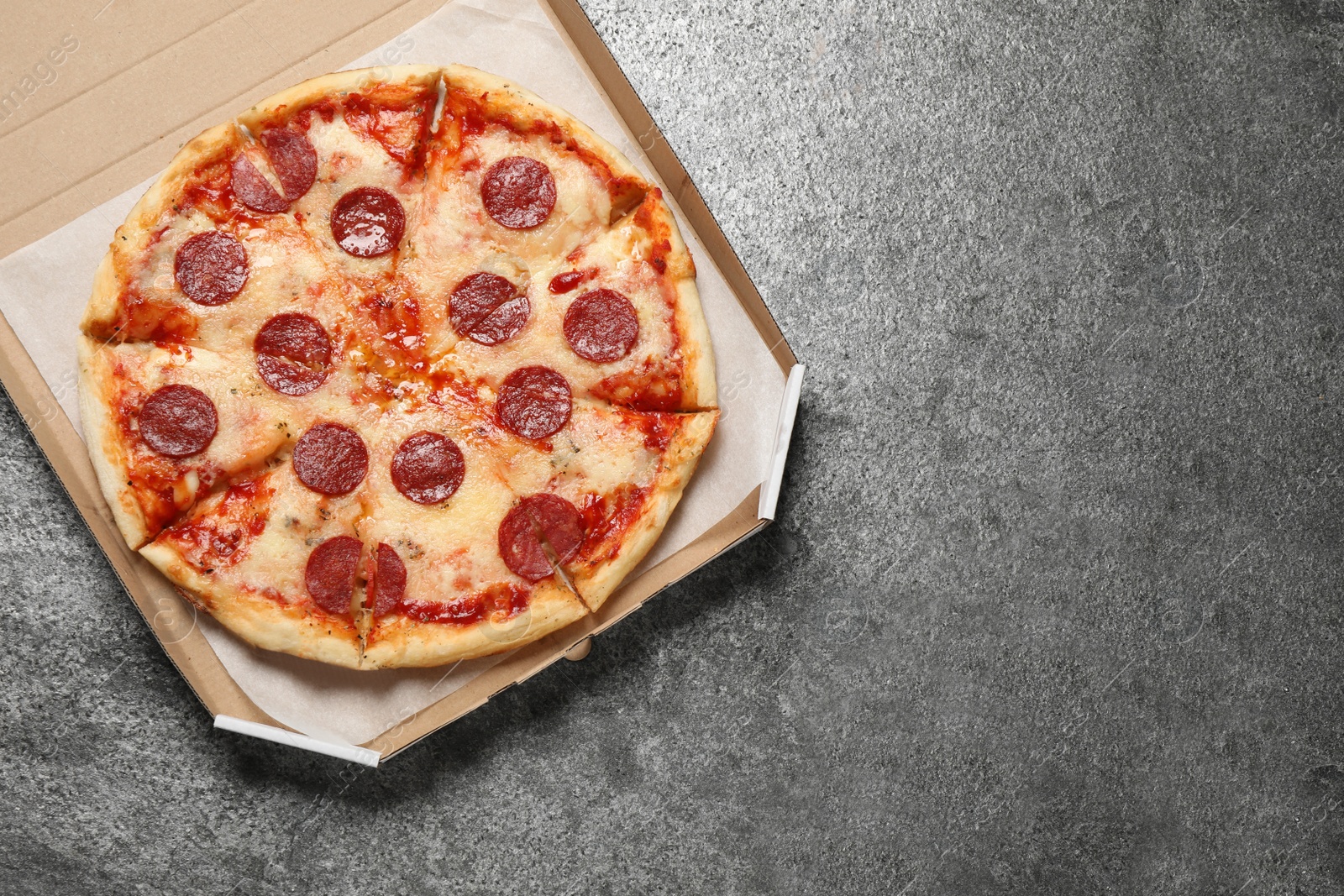 Photo of Hot delicious pepperoni pizza in cardboard box on grey table, top view. Space for text