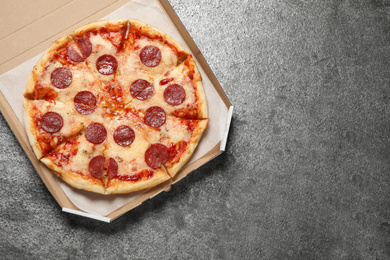 Hot delicious pepperoni pizza in cardboard box on grey table, top view. Space for text