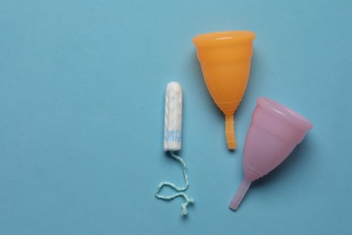Photo of Menstrual cups near tampon on light blue background, flat lay with space for text. Reusable and disposable feminine products