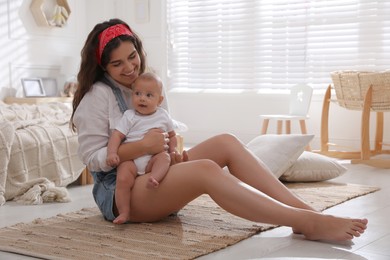 Happy young mother with her cute baby on floor in bedroom