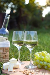 Photo of Delicious white wine, grapes, cheese and nuts on green grass outdoors