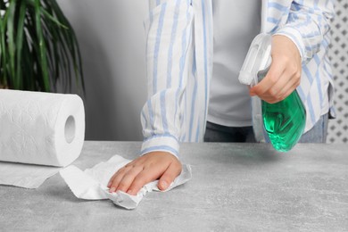Photo of Woman cleaning grey table with paper towel and detergent at home, closeup