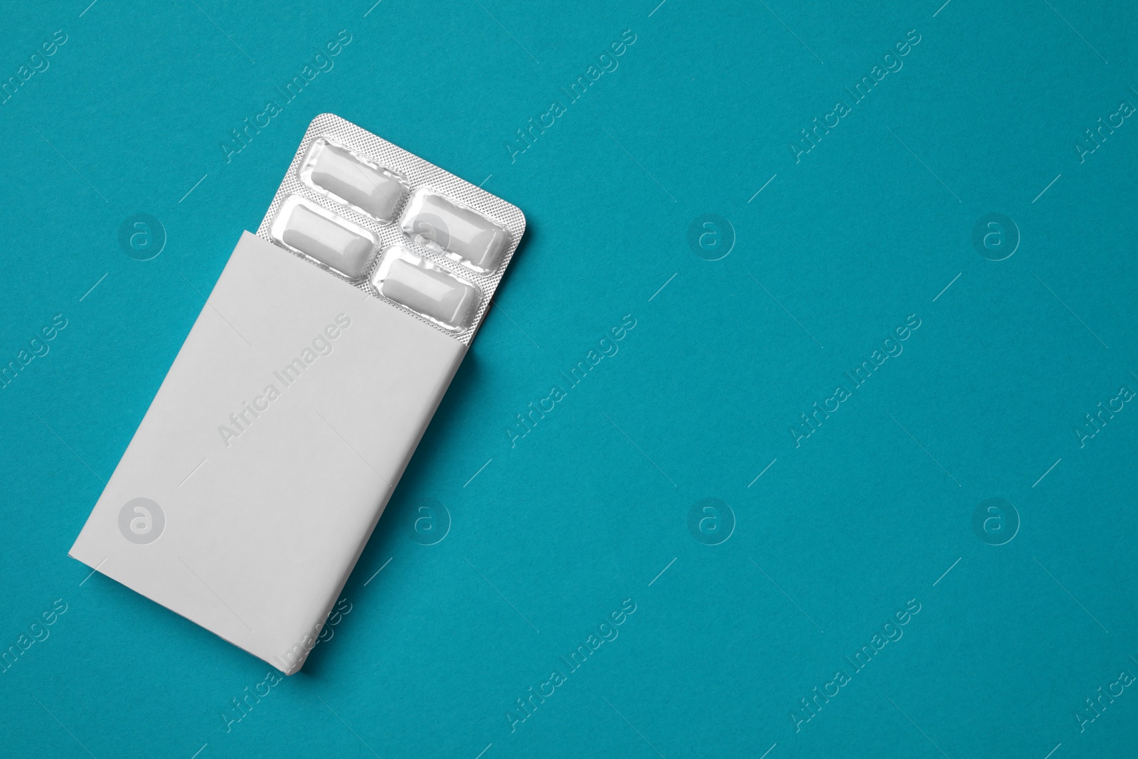 Photo of Pack with tasty chewing gums on turquoise background, top view. Space for text