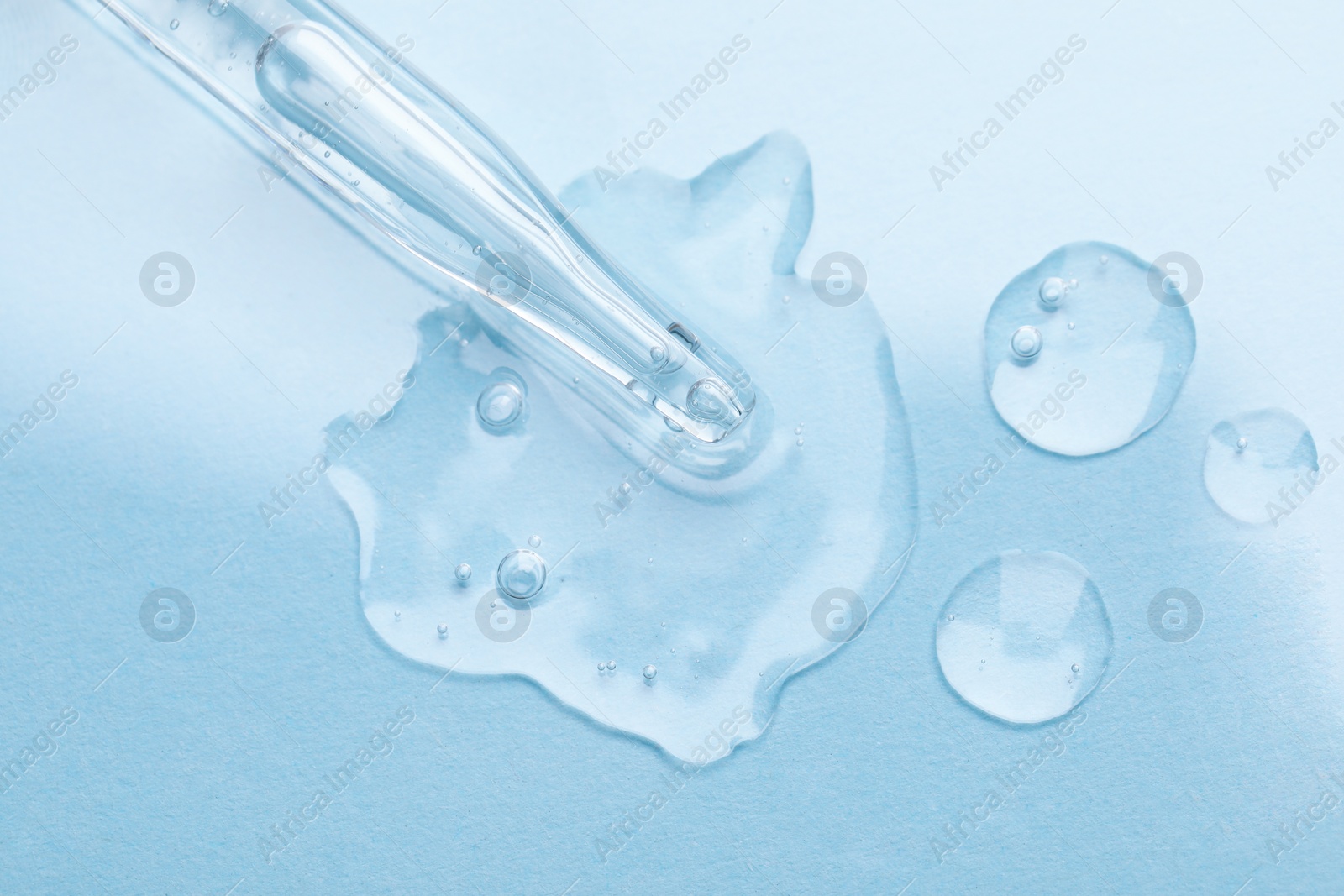 Photo of Glass pipette and transparent liquid on light blue background, top view