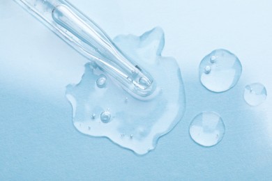 Photo of Glass pipette and transparent liquid on light blue background, top view