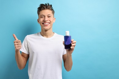 Photo of Young man with mouthwash showing thumbs up on light blue background, space for text