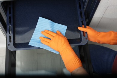 Young man cleaning oven tray with rag in kitchen, closeup