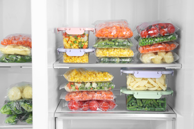 Plastic bags and containers with different frozen vegetables in refrigerator