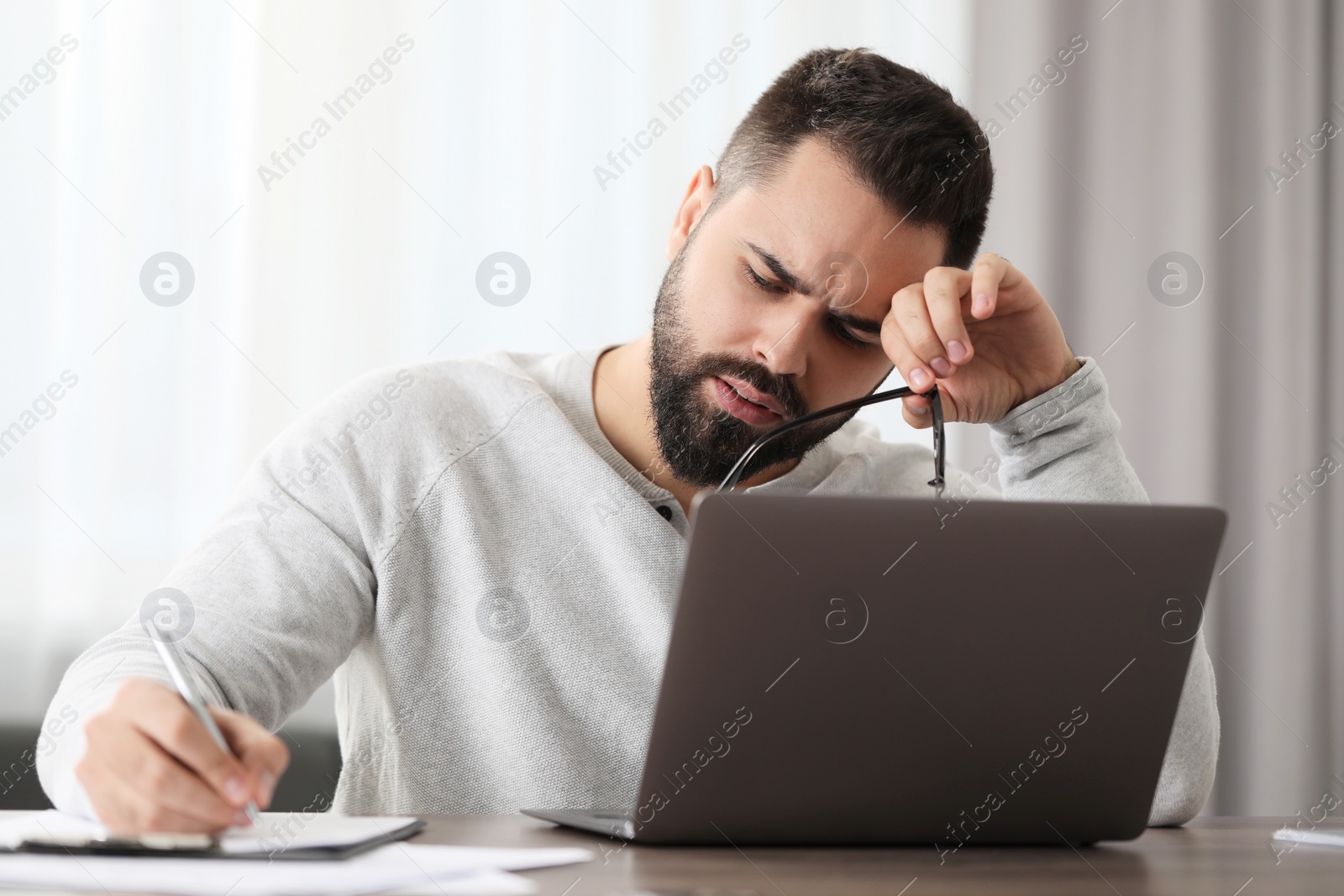 Photo of Man with glasses suffering from headache at workplace in office