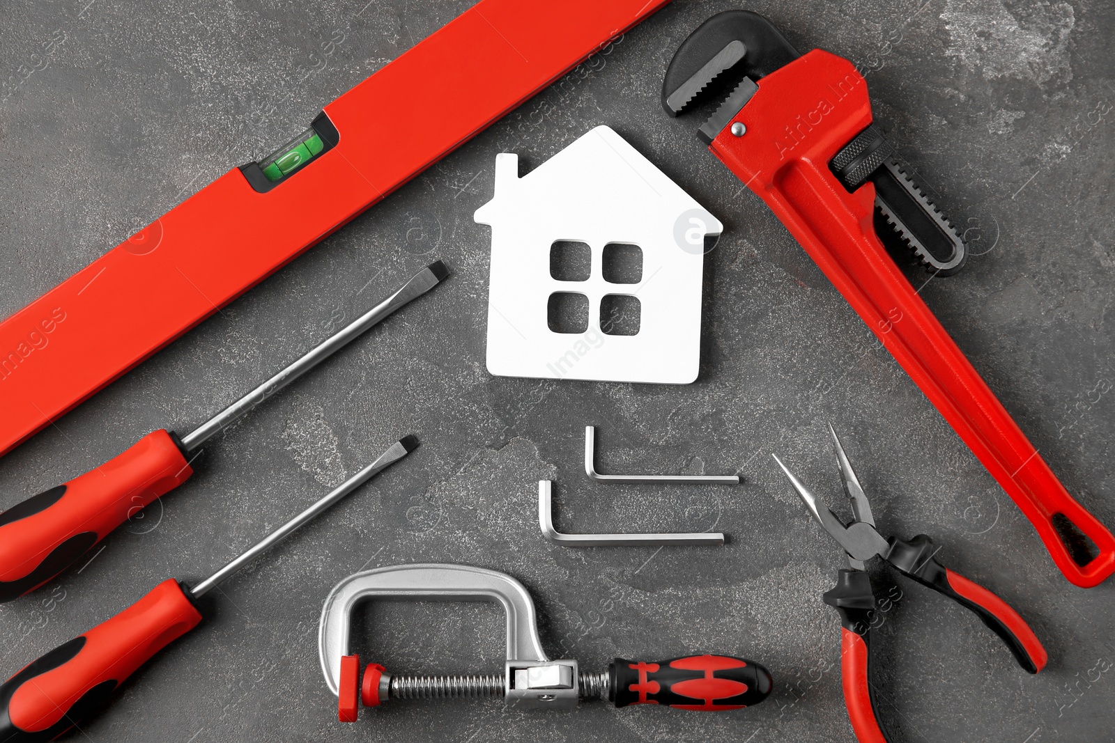 Photo of Set of repair tools and house figure on grey stone background, flat lay