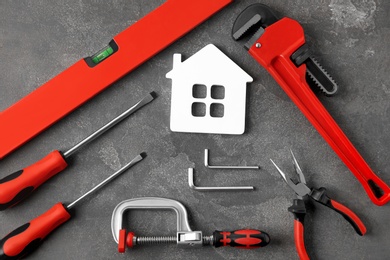 Photo of Set of repair tools and house figure on grey stone background, flat lay