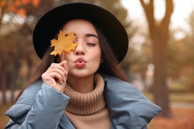 Photo of Young woman in stylish clothes holding yellow leaf outdoors. Autumn look