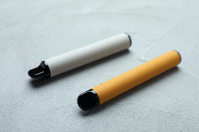 Photo of Disposable electronic cigarettes on grey table, closeup. Smoking alternative