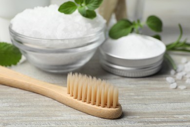 Toothbrush, sea salt and green herbs on wooden table, closeup