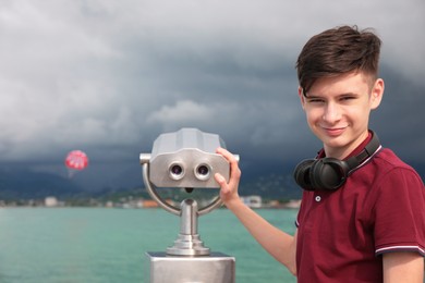 Photo of Teenage boy near mounted binoculars at sea. Space for text
