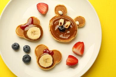 Creative serving for kids. Plate with cute bears made of pancakes, berries, banana and chocolate paste on yellow background, top view