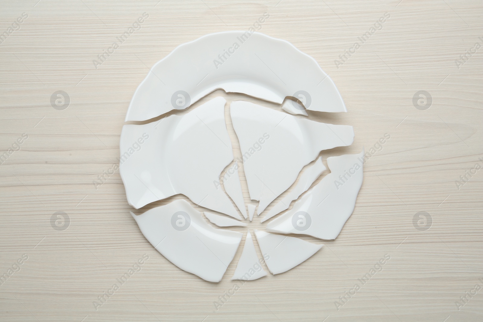 Photo of Pieces of broken ceramic plate on white wooden table, flat lay