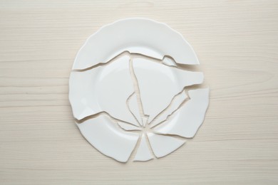 Photo of Pieces of broken ceramic plate on white wooden table, flat lay