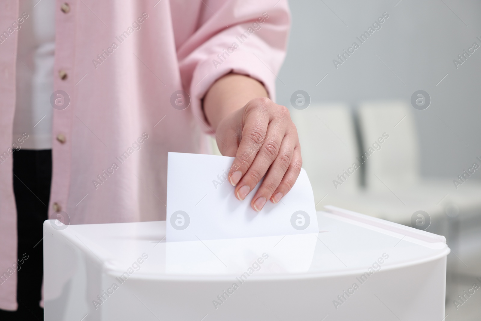 Photo of Woman putting her vote into ballot box on blurred background, closeup