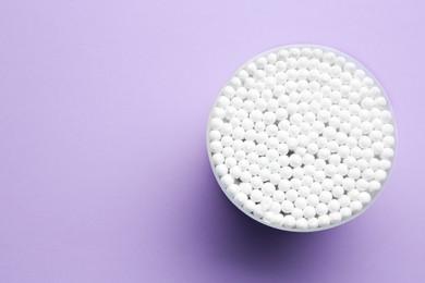 Photo of Many cotton buds in container on violet background, top view. Space for text