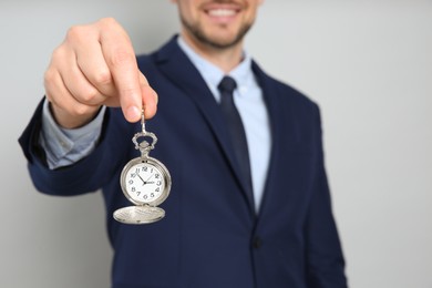 Photo of Happy businessman holding pocket watch on grey background, closeup. Time management