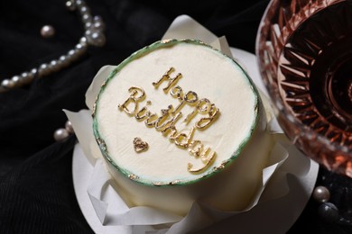 Delicious decorated cake with phrase Happy Birthday and glass of wine on black background