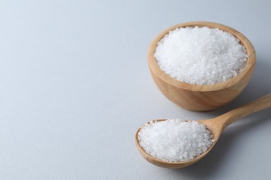 Photo of Organic white salt in bowl and spoon on light grey background, space for text