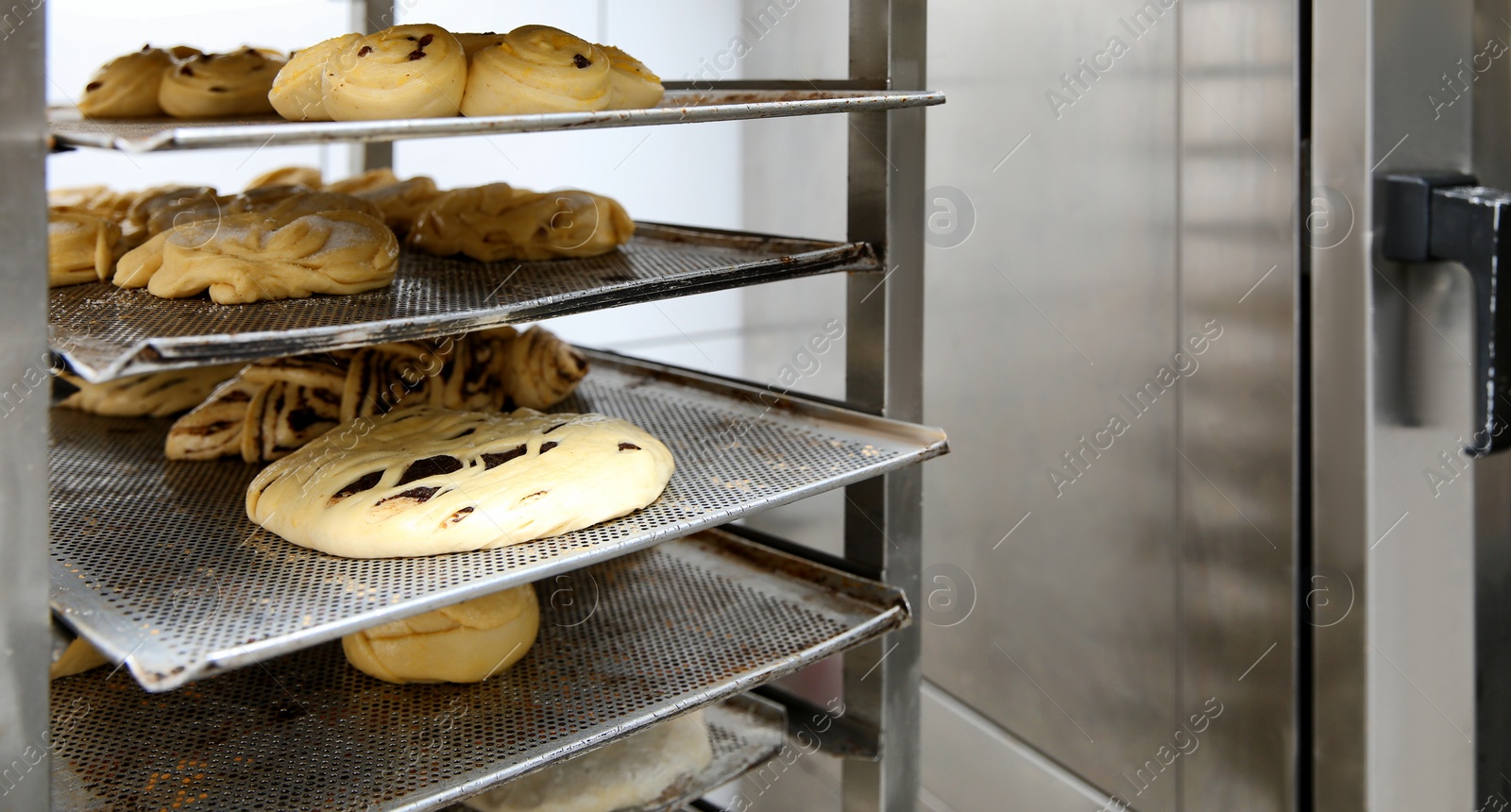 Photo of Rack with unbaked pastries in bakery workshop. Space for text