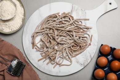 Photo of Uncooked homemade soba (buckwheat noodles) and ingredients on grey table, flat lay