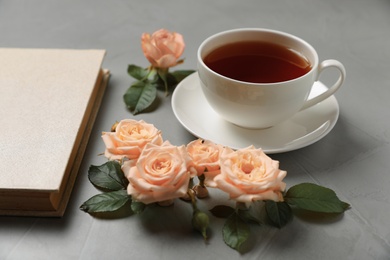 Photo of Hardcover book, flowers and cup of tea on grey table