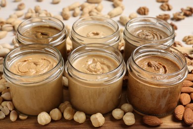 Many tasty nut butters in jars and nuts on table, closeup