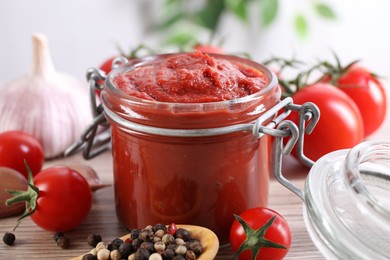 Photo of Jar of tasty tomato paste and ingredients on table, closeup