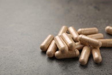 Photo of Dietary supplement capsules on grey table, closeup. Space for text