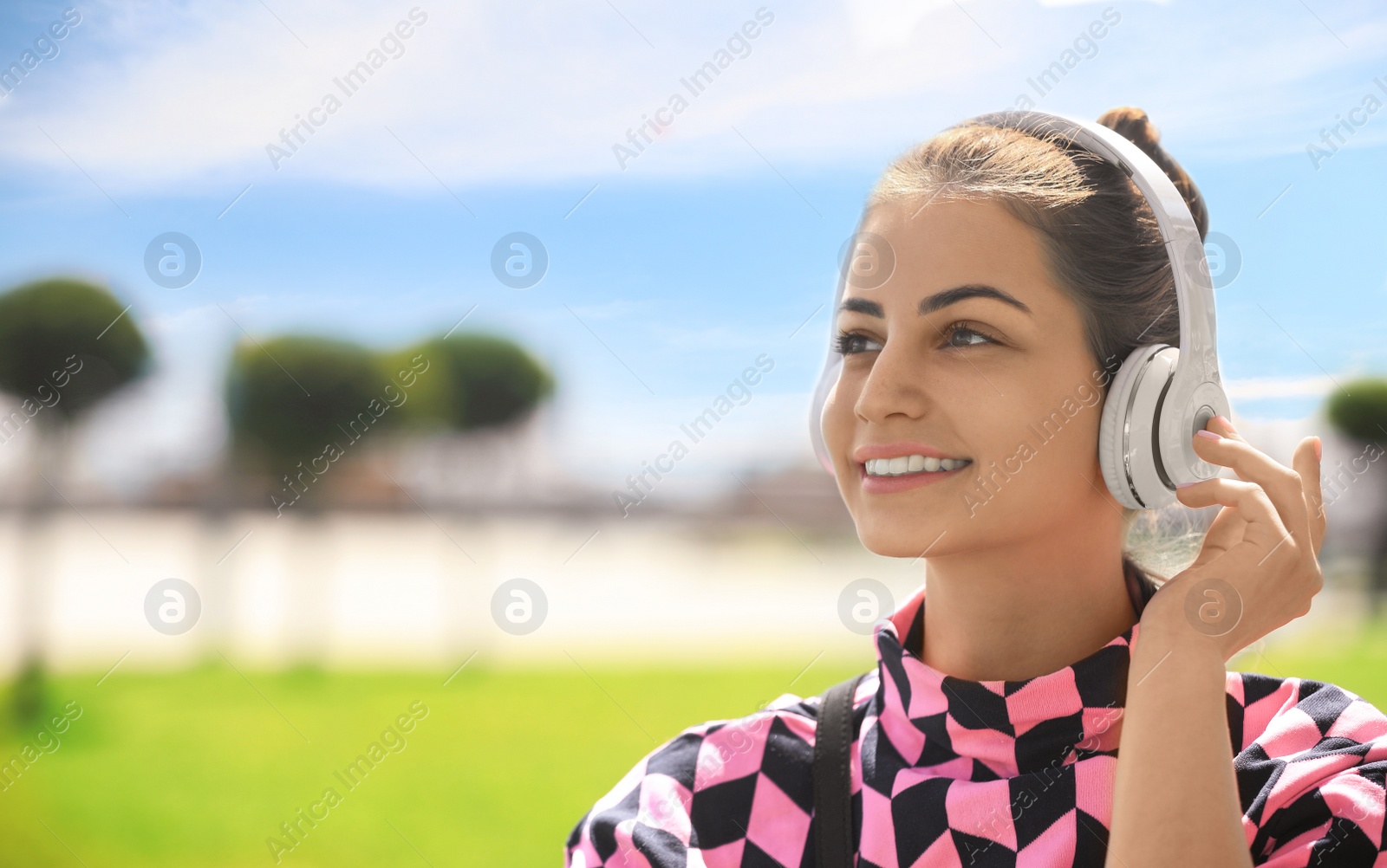 Photo of Young woman with headphones listening to music in park. Space for text