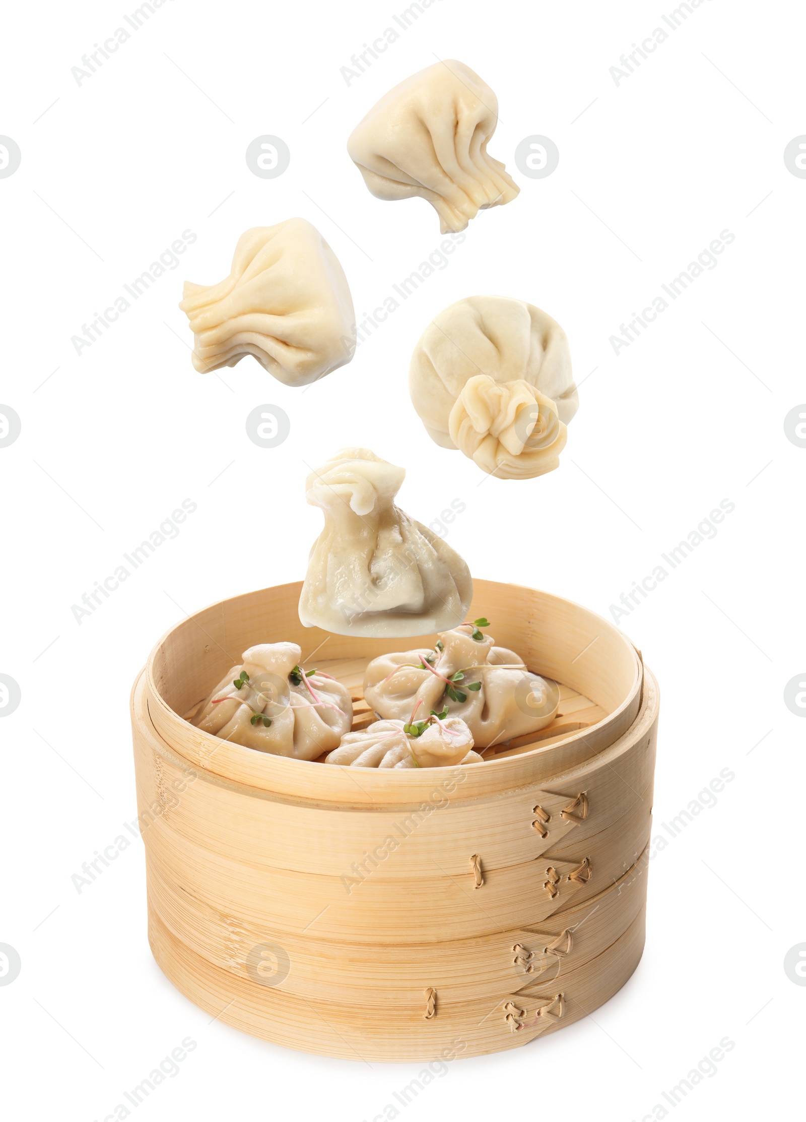 Image of Many tasty dumplings falling into bamboo steamer on white background