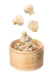 Image of Many tasty dumplings falling into bamboo steamer on white background