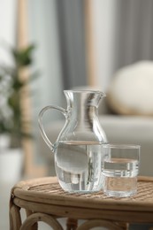 Jug and glass with water on wicker table against blurred background