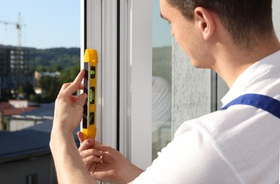 Photo of Worker using bubble level after plastic window installation indoors, closeup